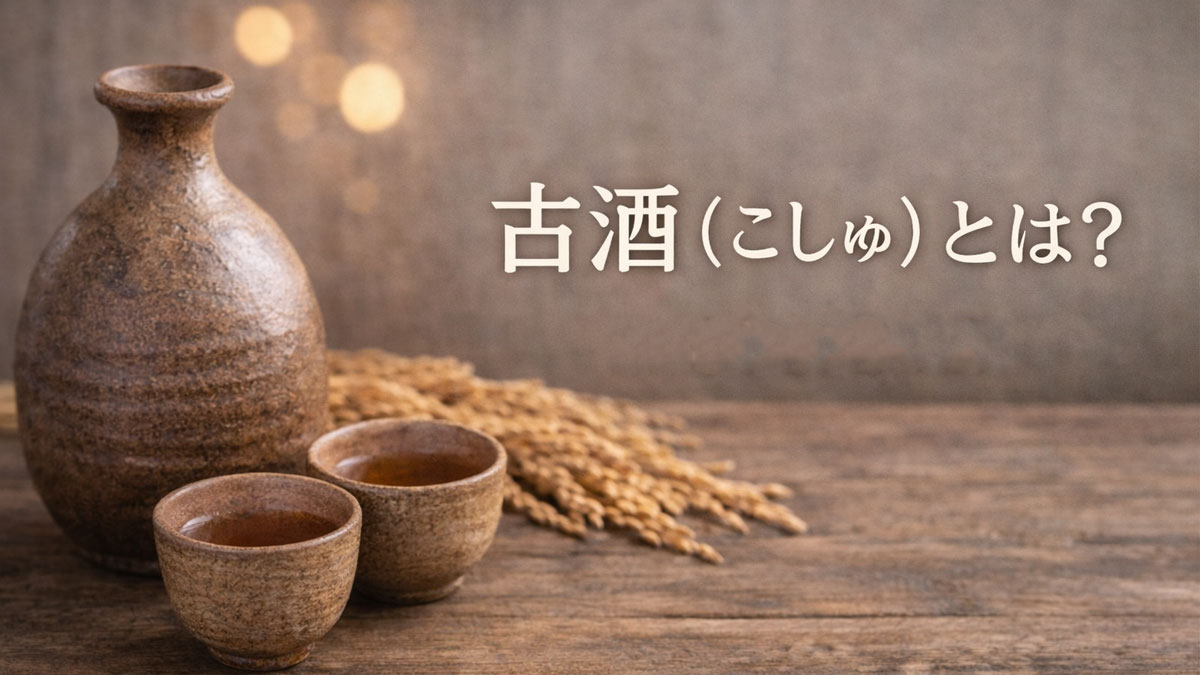 陶器の徳利とお猪口、琥珀色の古酒、稲穂を木のテーブルに並べ、「古酒(こしゅ)とは?定義と基礎知識」と日本語テキストを右側に配置した、ナチュラルで優しい雰囲気の解説イメージ画像